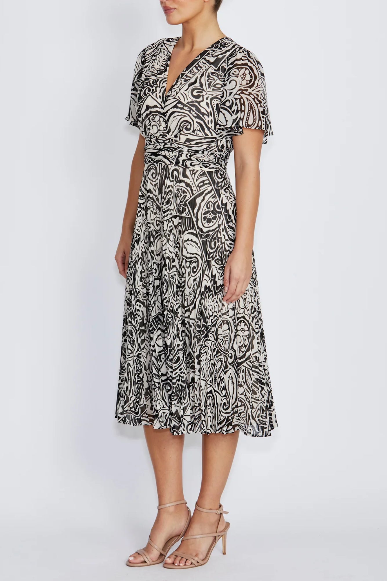 A woman wearing a black and ivory paisley midi dress walks down stone steps in front of a beige stucco wall.