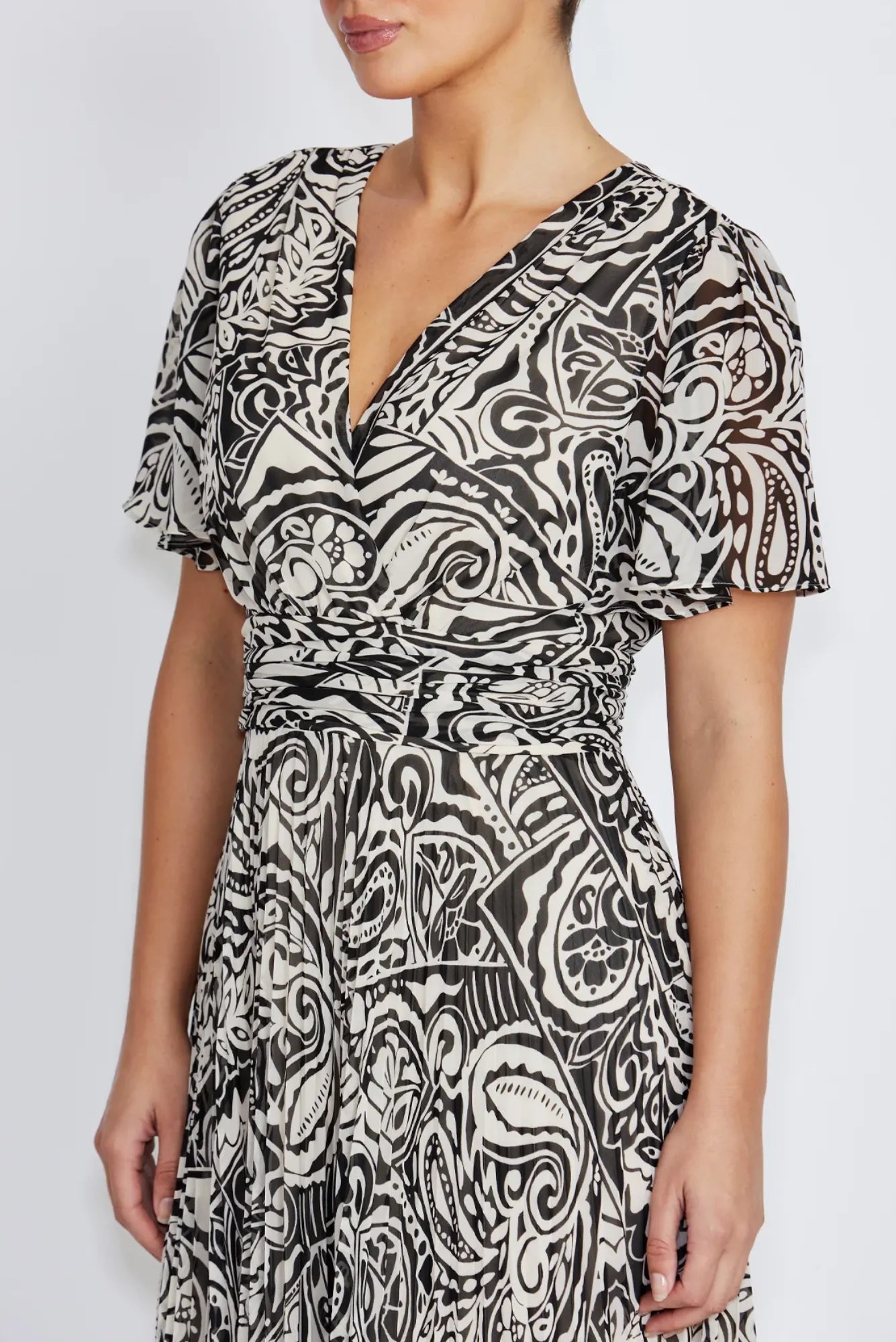 A woman wearing a flutter sleeve wrap dress with a black and off-white abstract paisley pattern, shown the waist detail  against a light gray studio background.